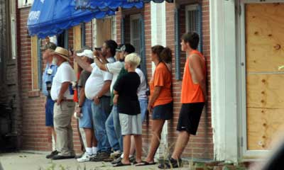 Group of people leaning against a wall, watching demolition equipment